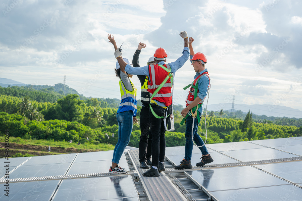 Poster construction workers in protective helmets are shaking hands while working on solar cell on roof fac