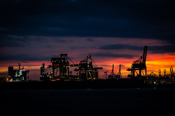 Fototapeta na wymiar The industrial landscape of the harbour in the Hook of Holland or Hoek van Holland in the Netherlands at sunset with cranes and machinery silhouetted against the setting sun