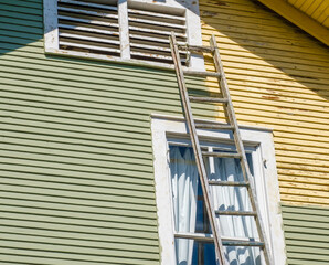 Ladder Leaning Against an Historic House with One Side Freshly Painted (Green) and the Other Side Not (Yellow)