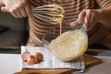 Senior woman beats eggs with flour for dough with a wisk in a glass bowl. Ingredients for a...