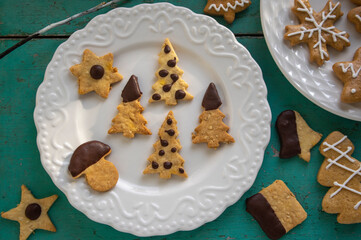 Painted traditional Christmas gingerbreads and custard cookies on white plates on old vintage painted table, various xmas shapes