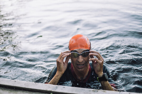 Mature man adjusting goggles while swimming in lake