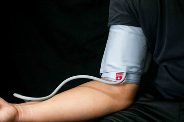 A man is using a blood pressure meter on his right arm on a black background.