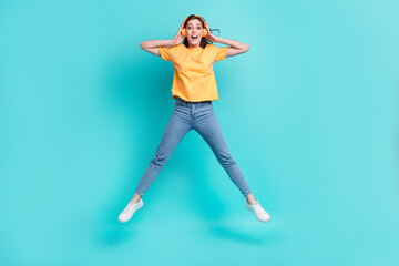 Full length photo of pretty impressed lady wear yellow t-shirt jumping high listening music isolated turquoise color background