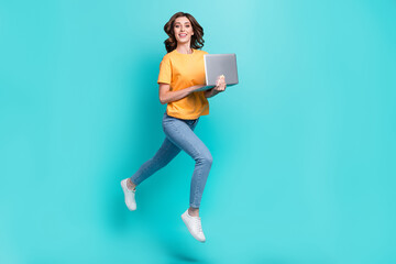 Full length photo of sweet pretty girl dressed yellow t-shirt jumping high typing modern device isolated teal color background