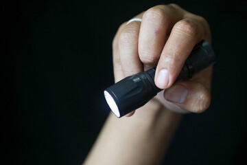 Close-up of a person's hand holding a flashlight on a black background.