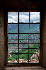 An ancient non-residential, stone city high in the Gamsutl mountains, against the backdrop of large, high mountains. View from the window with bars. Vertical Orientation