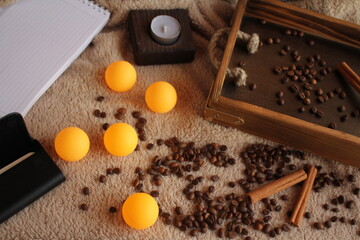 A lot of color ping-pong balls on the table. Coffee, a wooden tray with cinnamon, a candle and craft bags are scattered nearby. Morning. 