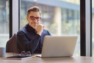 Business portrait - businessman using laptop computer in office. Happy middle aged man, entrepreneur working online.