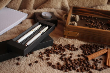 The pen is on the table. Coffee, a wooden tray of cinnamon, and a candle are strewn nearby. Morning. Postcard for the inscription of wishes.