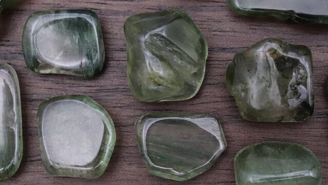 Green rutilated rare jewel stones texture on brown varnished wood background. Moving right seamless loop backdrop.