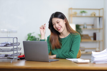 Beautiful Asian woman working on laptop and documents in home office.