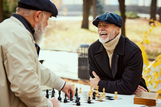 Portrait of two senior men playing chess in the park on a daytime in fall. Happy and delightful. Concept of leisure activity, old generation