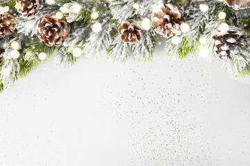 Christmas snowy fir tree branches, pine cone and bokeh garland on white background. Xmas greeting...