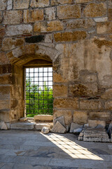 An old iron-barred arched window in a stone wall  and its shadow in the courtyard of the Isa Bey Mosque. 