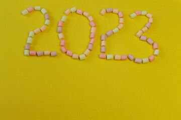 2023 is laid out of small multicolored marshmallows, yellow background, new year