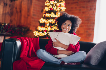 Full body portrait of cheerful minded little girl sit sofa hands hold cuddle cushion imagine newyear decor house indoors