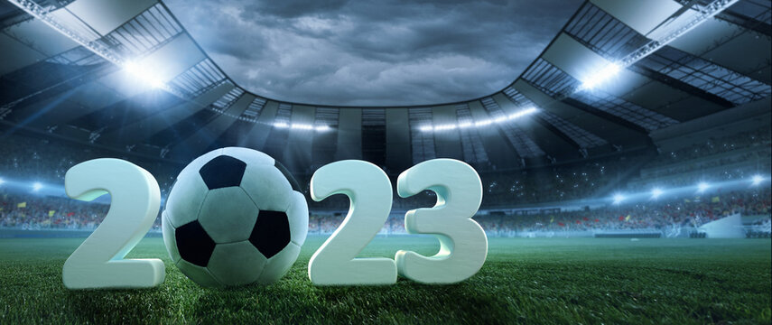Poster with soccer ball lying on grass of football field between huge numbers 2023 in crowded stadium with spotlight in evening. Concept of sport, energy, power