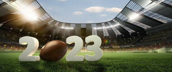 Leather american football ball on grass of football field between huge 3D numbers 2023 at stadium...