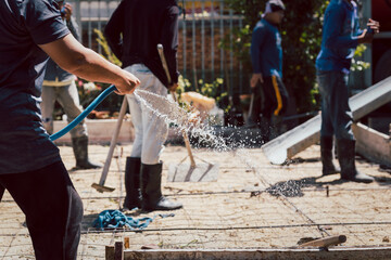 Worker watering ground preparing the concrete in the foundation.