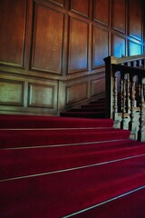Vertical shot of an old wooden staircase with red carpet