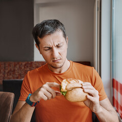 Frowned disgruntled man customer of a fast food restaurant digs into a burger and found a spoiled...