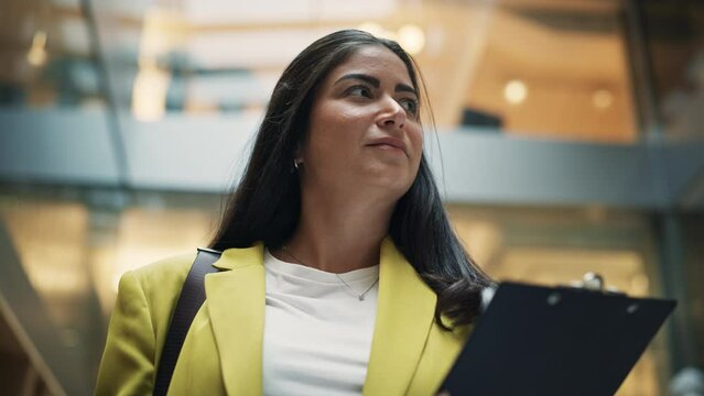 Portrait of Young Hispanic Female Lawyer Walking through the Hallway of a Corporate Office With Paper Holder in her Hands. Successful Female Human Resources Agent Checking her Inspection Documents