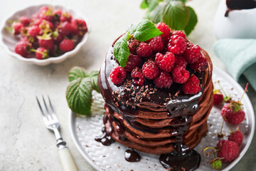 Chocolate Pancakes. Pancakes with fresh raspberry with chocolate glaze or toppings in gray bowl on light gray table background. Homemade classic american pancakes. Page for magazine concept.