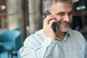 Gray-haired middle-aged man in stylish shirt is talking on mobile phone