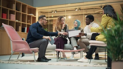 Multiethnic Youthful Group of People Preparing a Presentation in a Casual Conference Room at Office. Startup Data Team Discussing Process Using Laptop and Charts. Zoom Out Wide Shot - Powered by Adobe