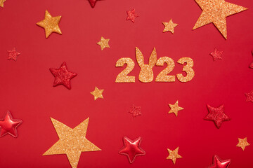 2023 new year flat lay concept. Numbers 2023 with red and gold stars and rabbit, top view on red background