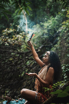 Imagen vertical de una mujer afroamericana sentada sola en medio del bosque en sinton&iacute;a con la naturaleza por medio de un  ritual de meditaci&oacute;n. 