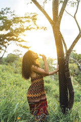 Imagen vertical de una mujer afroamericana de pie al lado de un árbol al aire libre realizando un...