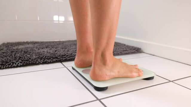 Woman checking her weight by stepping onto a bathroom scale.