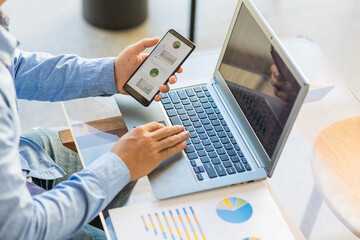Asian businessmen use equipment for business. Holding a smartphone that works with laptops and mobile phones, showing statistics and software apps.