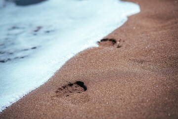 Pair of footprints on the beach sand, almost erased by the waves