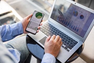 Businessman using gadgets for business, Asian office worker holding smartphone working with laptop and mobile phone, statistical apps and company software, looking over shoulder