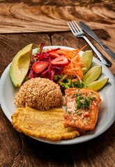 Vertical shot of a white plate with salmon, rice, and vegetable salad on a wooden table