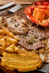 Vertical shot of grilled pork steaks, fries, and vegetable salad on a wooden table