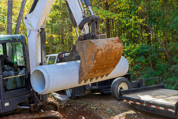 An excavation worker uses tractor to lift concrete sewage pipes from trucks placed on ground to prepare for underground installation