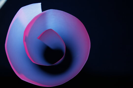 Rollo de papel blanco de impresoras 3D en c&igrave;rculos con luz azul y rosa forma un embudo en degrad&egrave; con sombra, presenta una figura abstracta de bordes suaves  formando un bello dise&ntilde;o con fondo negro