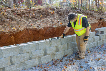 Man levels tool during construction of concrete block retaining wall on new property that is being built