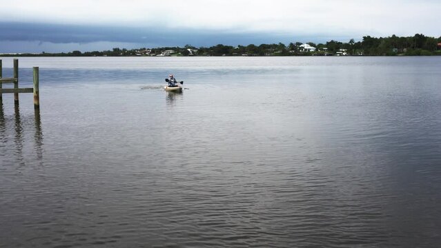 An elderly man in sun protection wears a kayak down a river in Florida approaching the camera