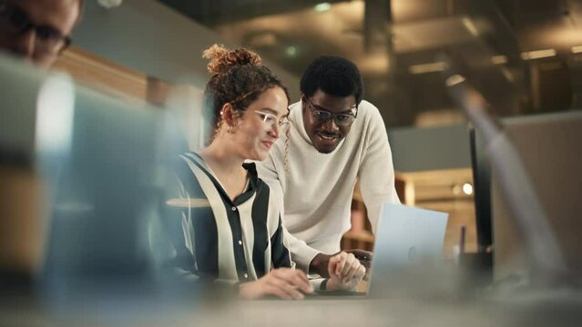 Portrait of Two Creative Colleagues Using Laptop to Discuss Work Project at Office. Young Black Technical Support Specialist Helping Female Customer Relationship Coordinator. Teamwork Concept