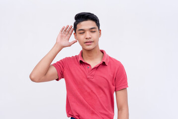 A young asian man listening on the latest gossip. Hand gesture on ear. Isolated on a white background.