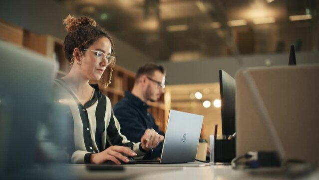 Portrait of Enthusiastic Hispanic Young Woman Working on Computer in a Modern Bright Office. Confident Human Resources Agent Smiling Happily While Collaborating Online with Colleagues. Dolly Shot.