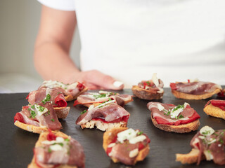 Ham and red bell pepper appetizer on bread. Woman's hand serving food holding blackboard tray. Concept of pinchos and tapas, typical Spanish food.