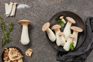 King Oyster mushrooms or Eringi in a bowl and dried white mushrooms on a dark background.  Flat lay.