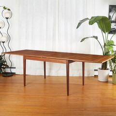 Mid-century Modern Double Flip Top Teak Table. Product photograph of a beautiful vintage table before a white curtain, lively houseplants, and a futuristic lamp. 
