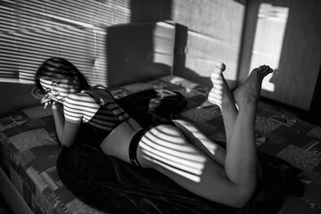 Gorgeous slim woman lies on the bed and relaxes under sun rays. Black and white snapshot of an attractive lady.